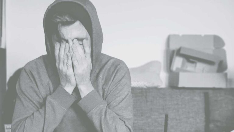 Man in hoodie has his face in his hands looking upset