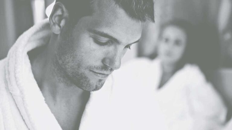 Close up view of man in white dressing gown with woman blurred in background