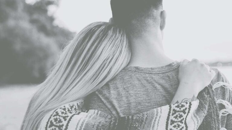Rear view of a blonde haired woman with her arm over her boyfriend's shoulder