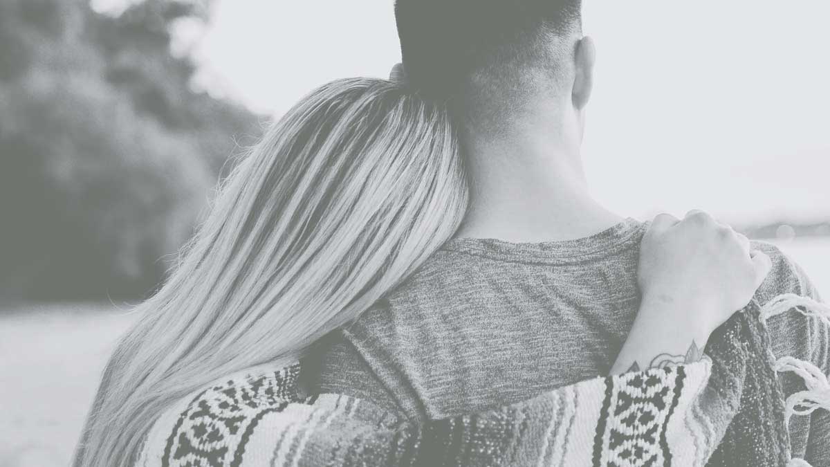 Rear view of a blonde haired woman with her arm over her boyfriend's shoulder