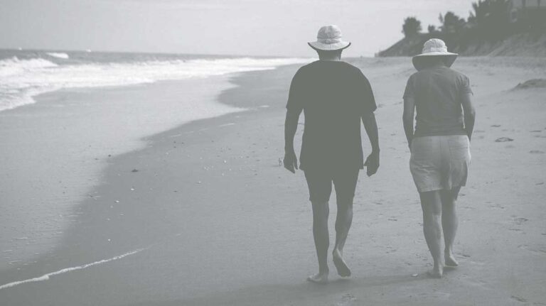 A couple walk on a beach with their backs to the camera